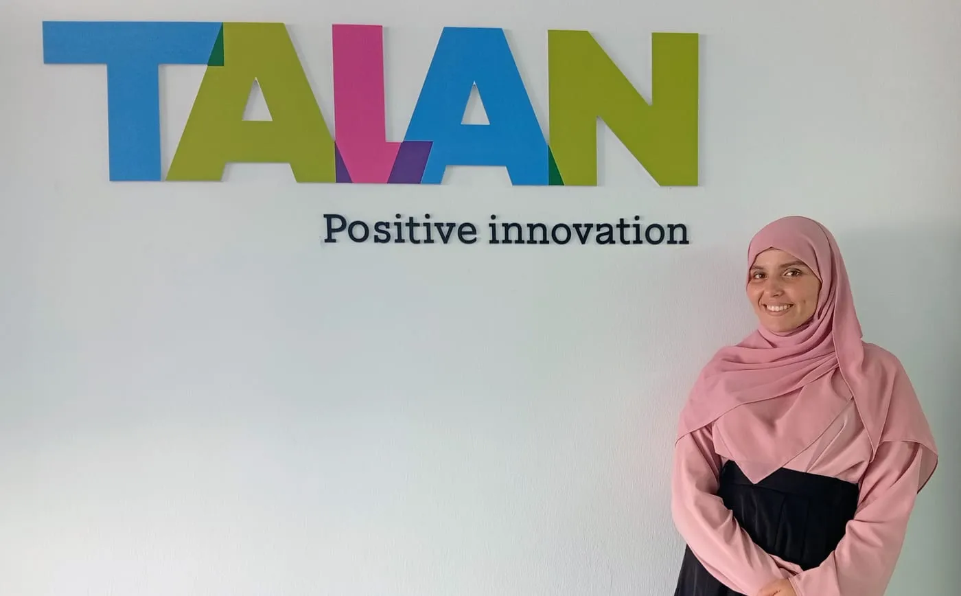 Ines smiling by the Talan “Positive innovation” logo wall in Tunis